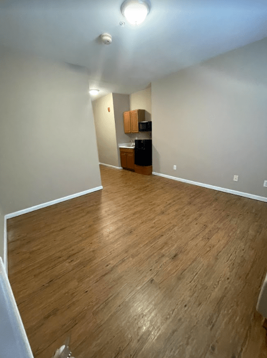 A view of a spacious apartment interior with wood flooring and an adjoining kitchen area.