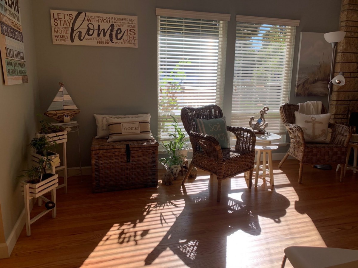 A cozy living room filled with natural light, featuring rattan furniture and indoor plants.