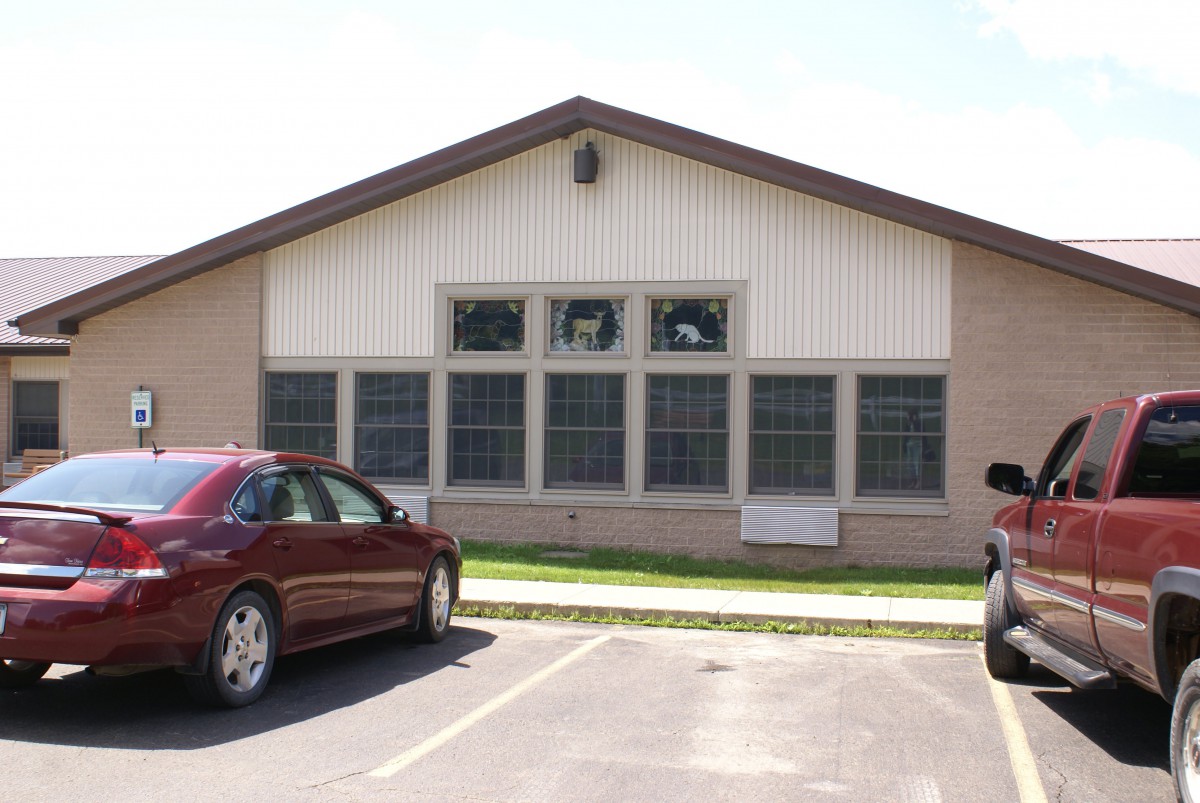 A small building with a parking lot and parked cars on a sunny day.