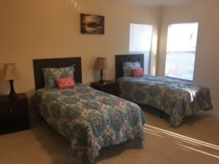 A cozy bedroom with two twin beds adorned with patterned bedspreads, a shared bedside table, and a lamp by the window.