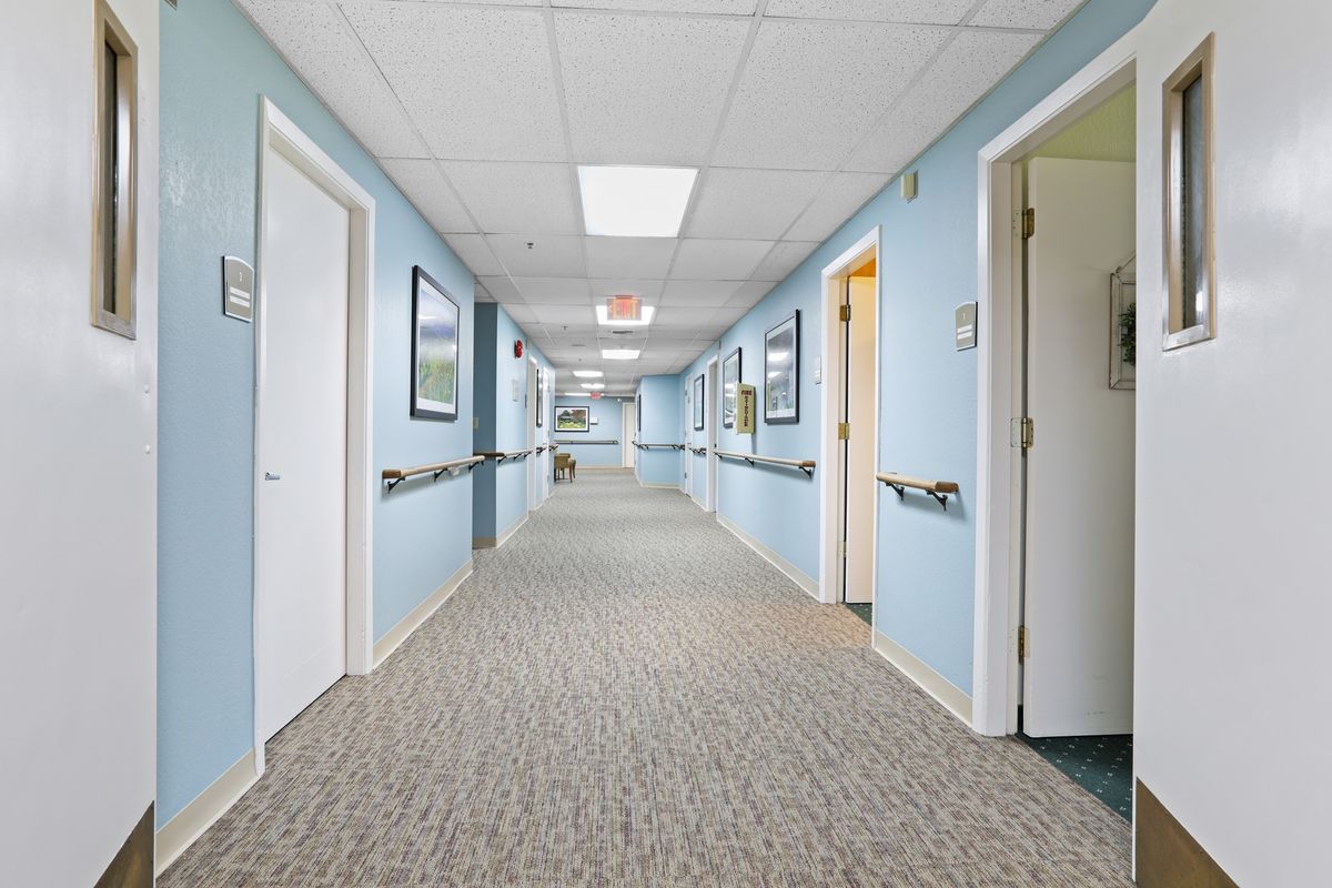A clean and quiet hospital hallway with blue walls and multiple doors.