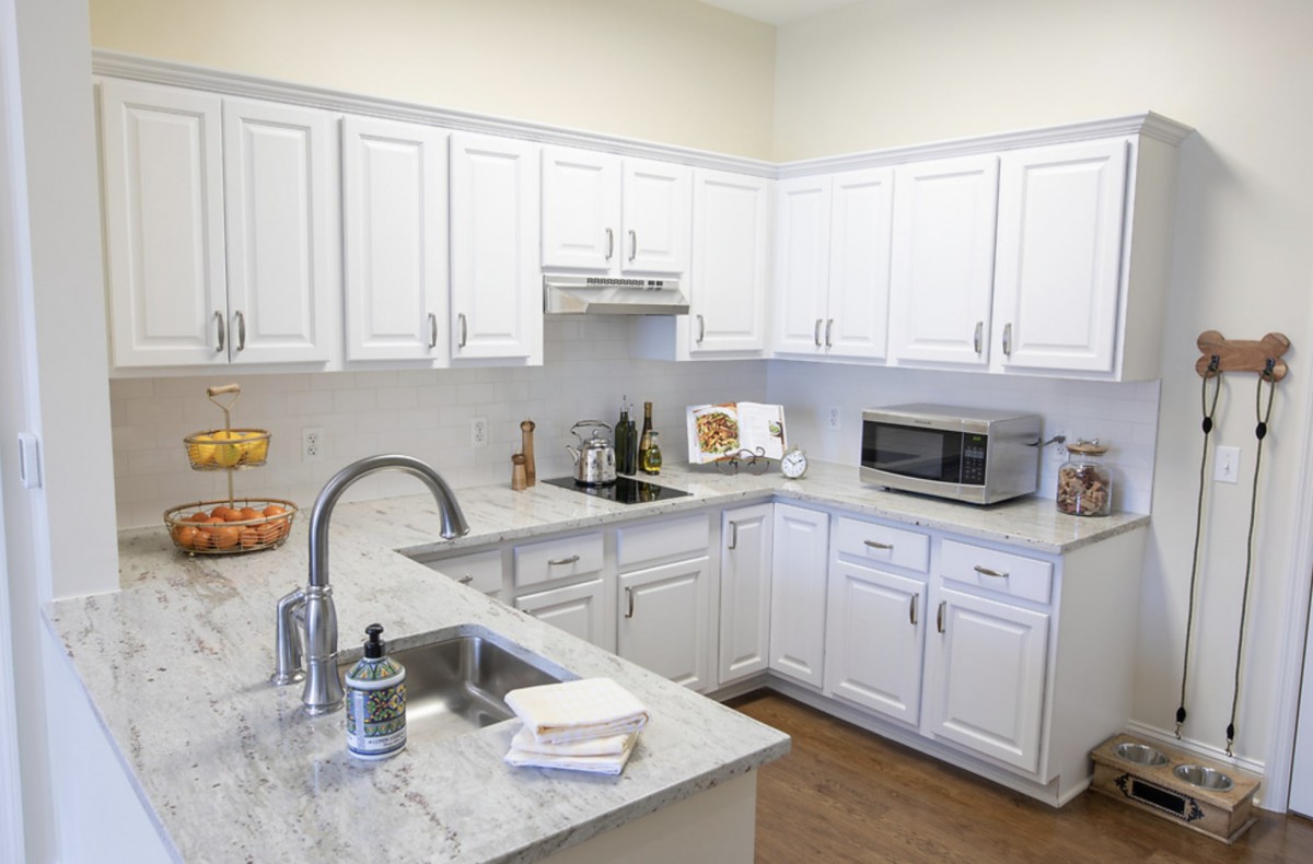 A clean and modern kitchen with white cabinets and countertops, featuring a microwave and sink.