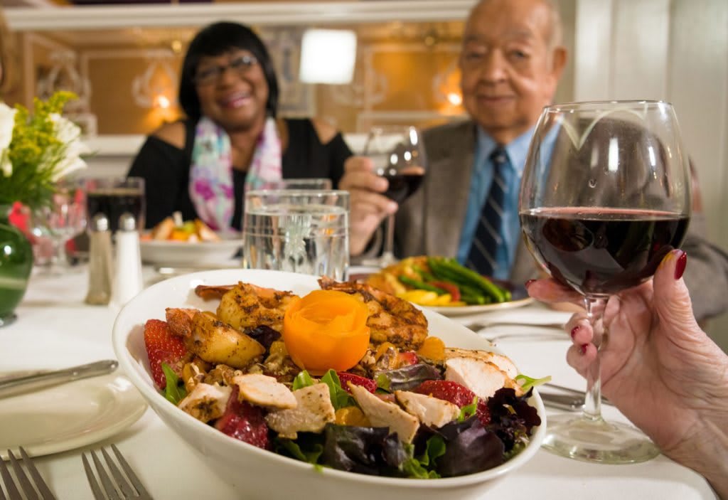 A couple enjoying a meal with wine at a restaurant, featuring a diverse salad in the foreground.