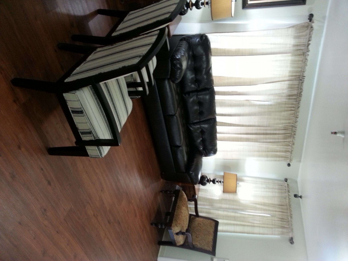 A cozy living room with a black leather sofa, striped chairs, and elegant lighting.