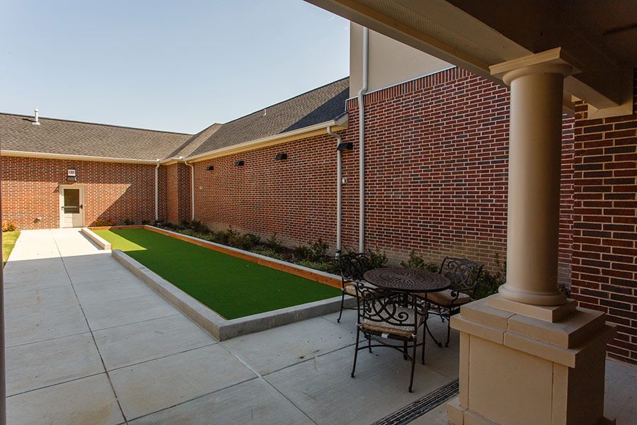 A cozy courtyard with brick walls, featuring a small patio set and an artificial grass area.