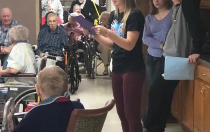 A caregiver reads to a group of elderly individuals in a nursing home setting.