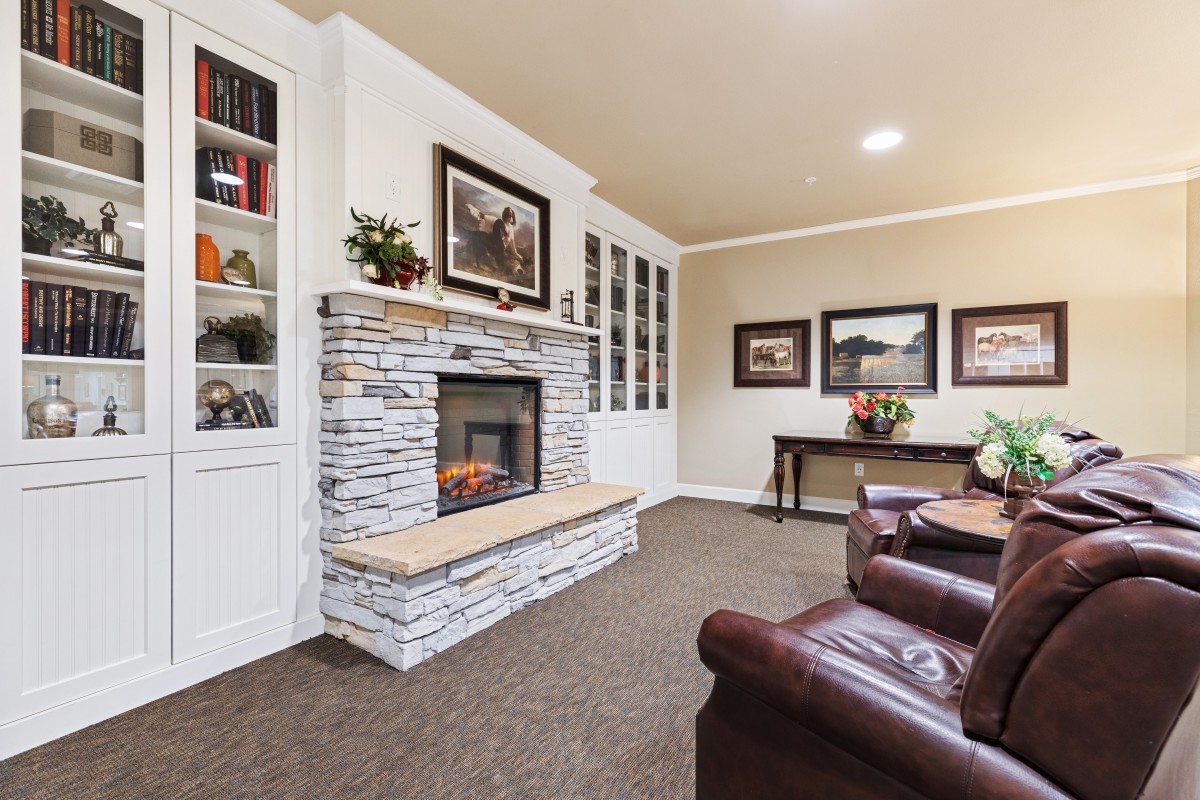 A cozy living room with a stone fireplace, leather armchairs, and built-in bookshelves.