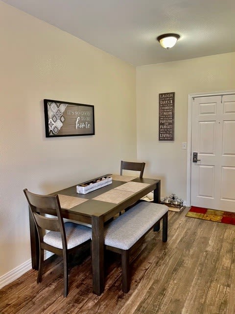 A cozy dining area with a wooden table, chairs, and bench seating, adorned with minimalist wall art and warm wood flooring.