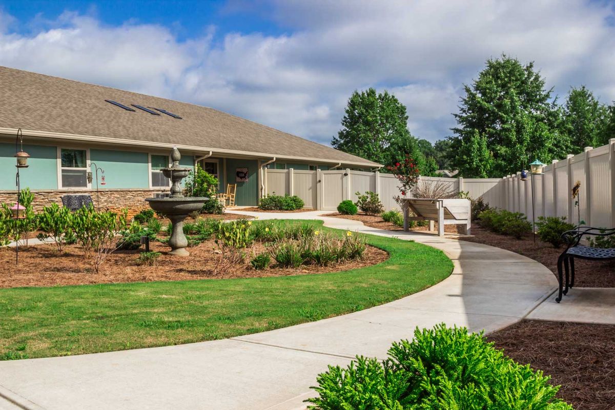 A well-maintained garden with a curved pathway leading to a house, surrounded by lush greenery and colorful plants.