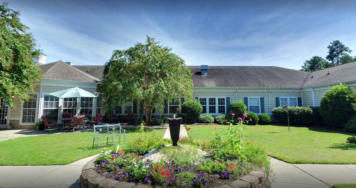 A beautiful garden with a central fountain in front of a house.