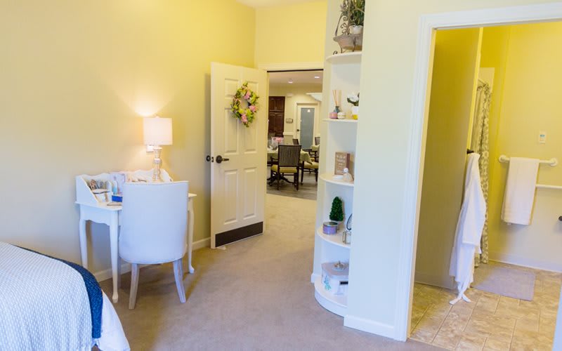 A cozy bedroom with a desk and lamp, leading into a hallway.