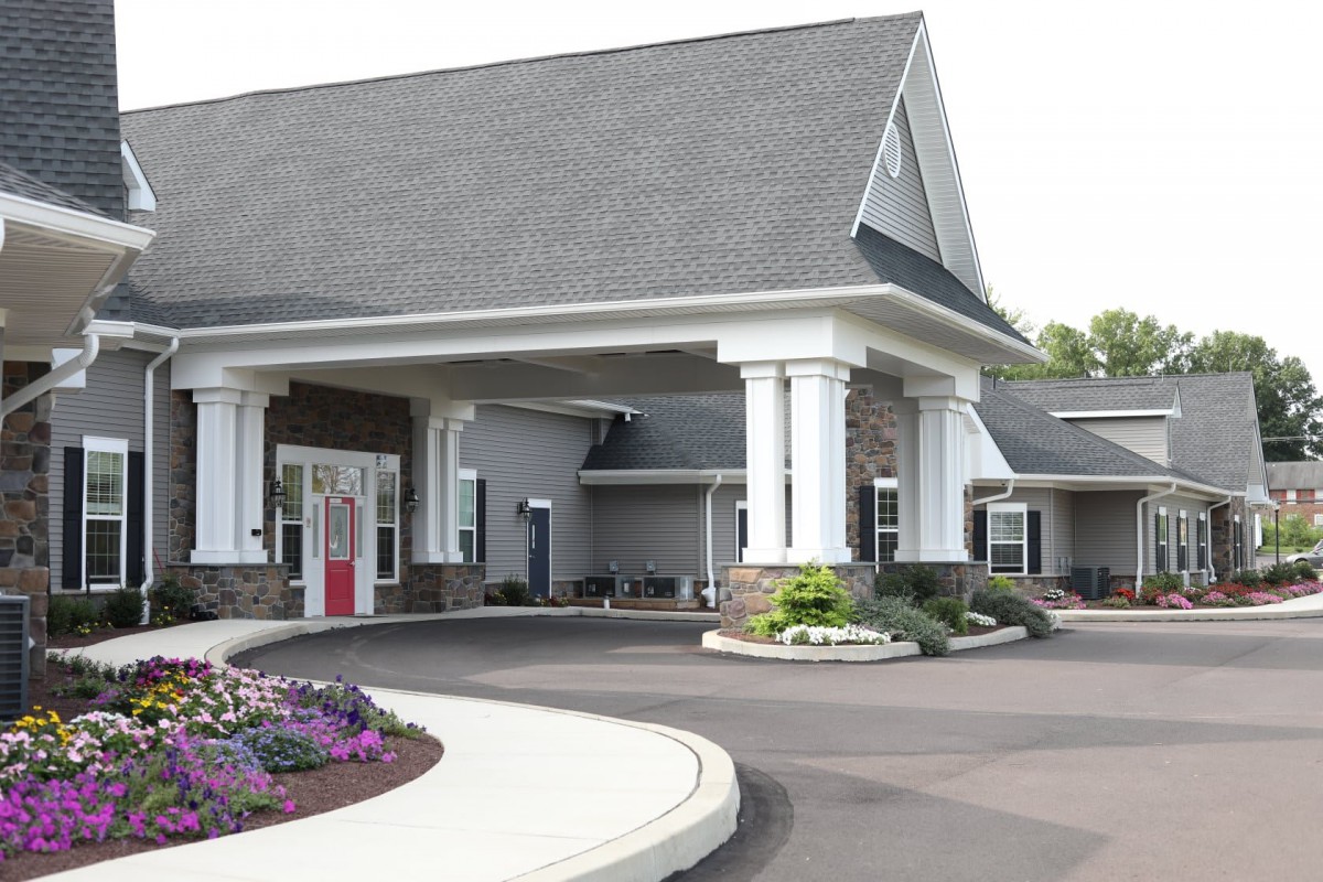 The image shows the entrance of a modern building with landscaped surroundings and prominent columns.