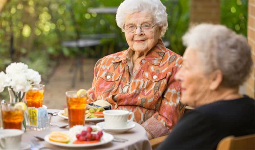 Two elderly women enjoying an outdoor meal together.