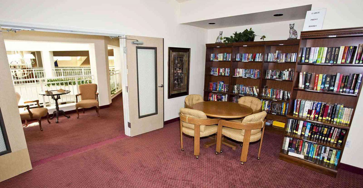 A cozy reading area in a library with bookshelves, a round table, and chairs on a carpeted floor.