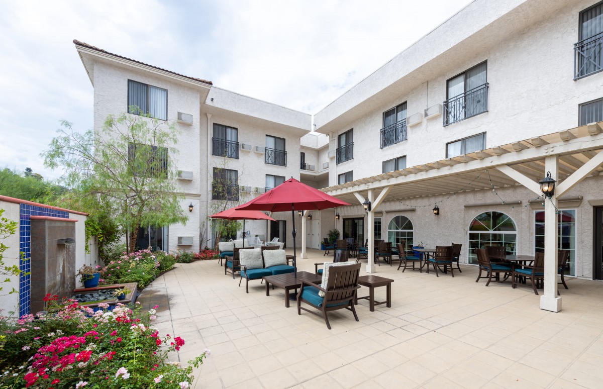 Outdoor patio area with seating and a red umbrella in front of a modern building.
