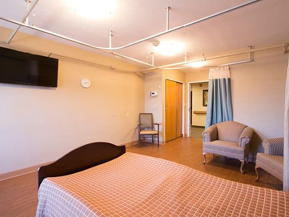 A clean and spacious hospital room with a bed, TV, and comfortable seating.