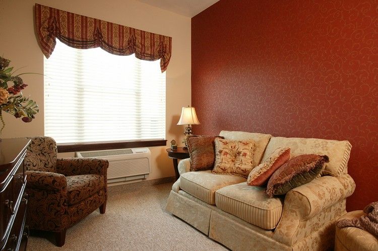 A cozy living room with a sofa, armchair, and a lamp beside a window with curtains.
