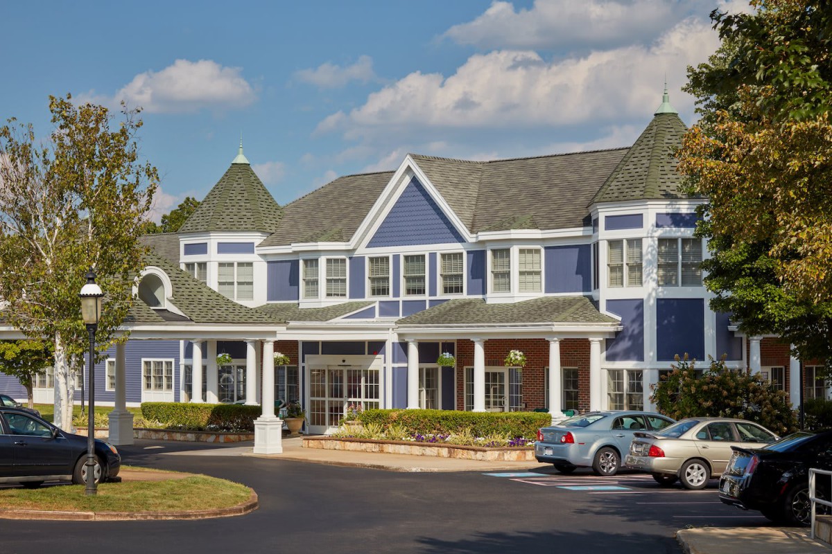 A two-story blue residential building with a driveway and parked cars.