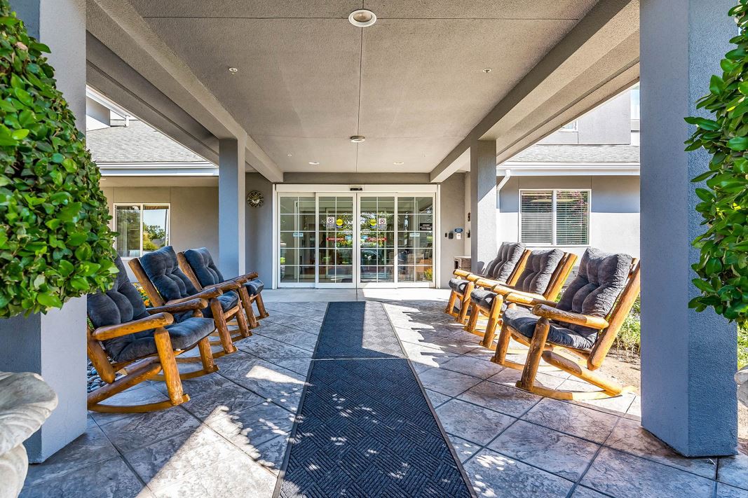 A covered patio with wooden rocking chairs arranged in rows, creating a cozy outdoor seating area.