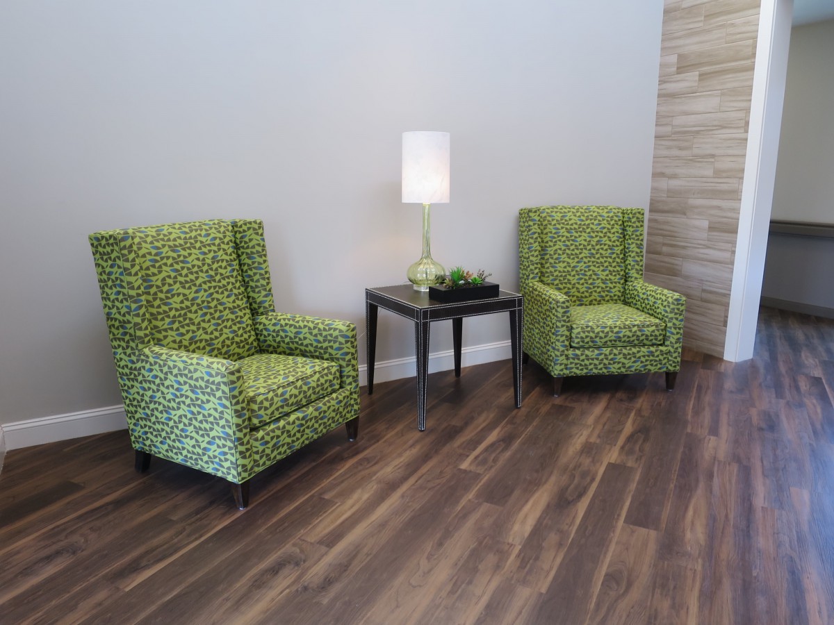 A cozy living space featuring two green patterned chairs, a small black table, and a modern lamp on a wooden floor.