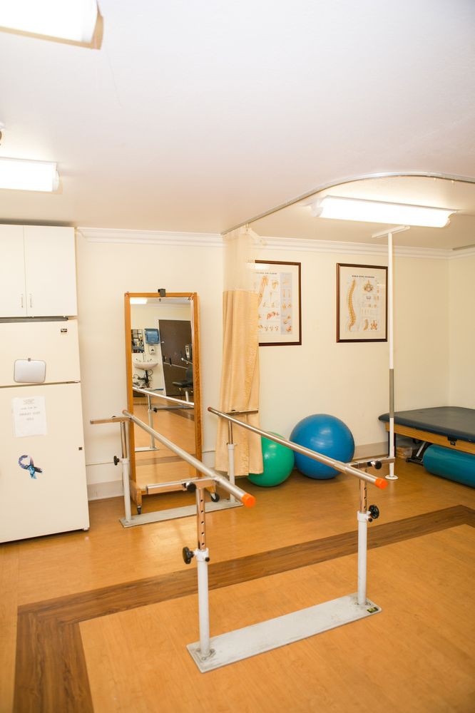 A well-equipped physical therapy and rehabilitation room featuring parallel bars, a large mirror, therapy balls, and other exercise equipment.