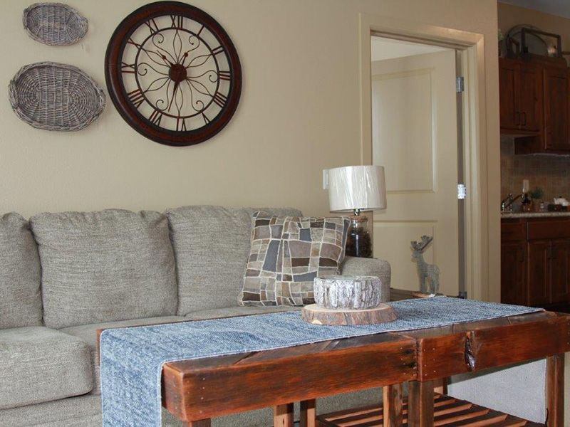 A cozy living room with a sofa, decorative wall clock, and a table with a lamp.