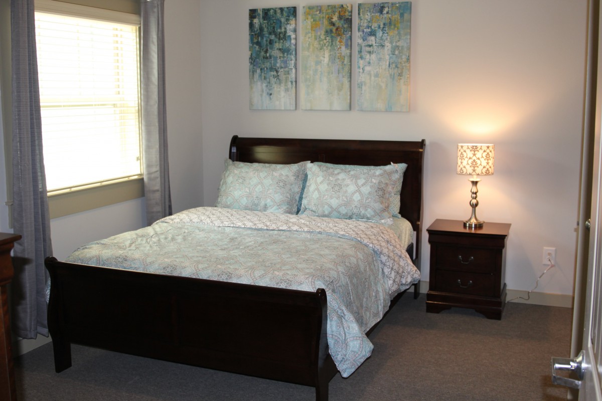 A cozy bedroom with a neatly made bed, nightstand, and ambient lighting.