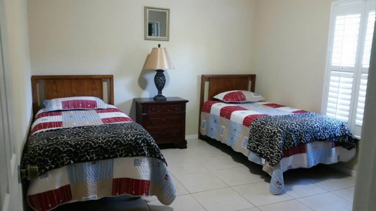 A simple bedroom featuring two twin beds with colorful quilts, a central nightstand, and a lamp.