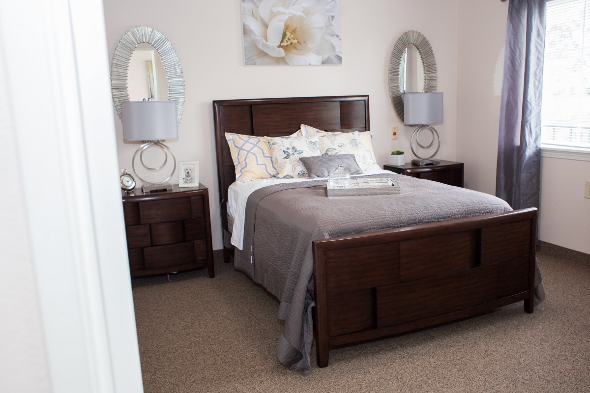 A neatly arranged bedroom with a stylish bed, nightstands, and decorative mirrors.