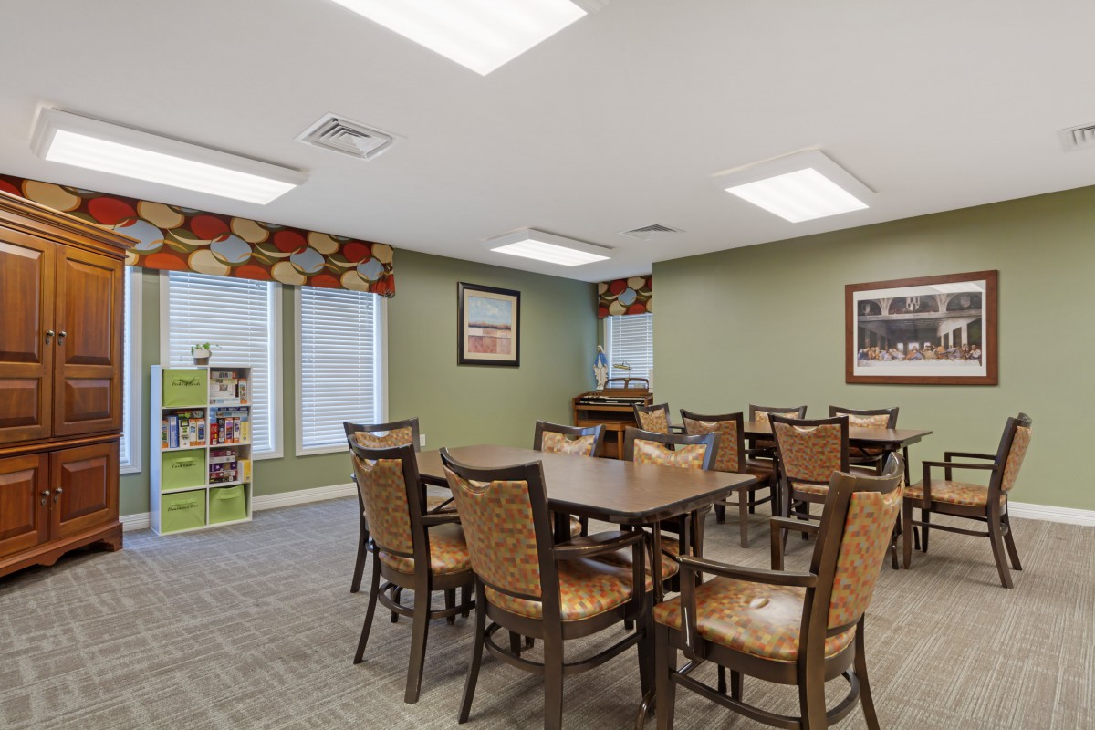 A well-lit indoor dining area with neatly arranged tables and chairs, featuring decorative windows and wall art.