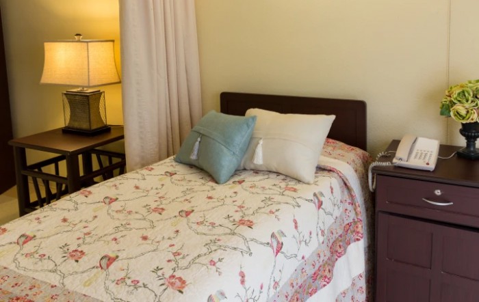 A cozy bedroom with a neatly made bed featuring decorative pillows and a floral quilt, accompanied by a warm glowing lamp.
