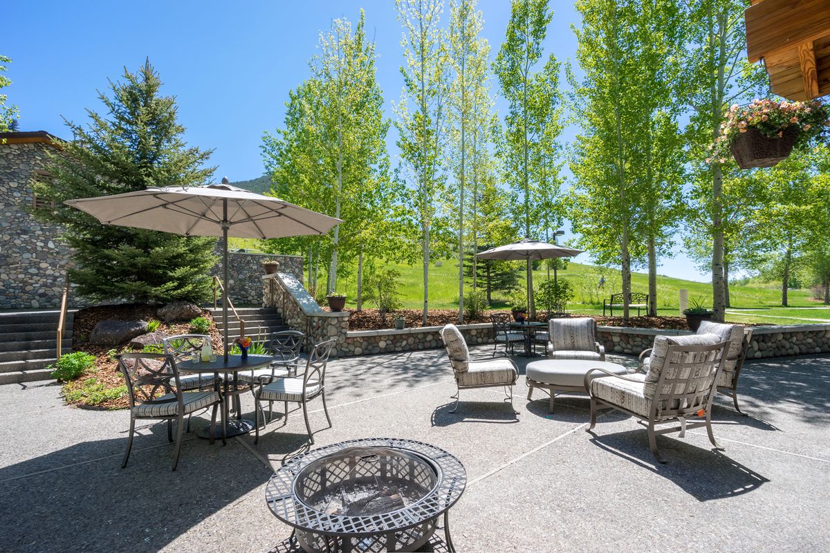 A sunny outdoor patio area with seating, tables, and umbrellas surrounded by lush trees.