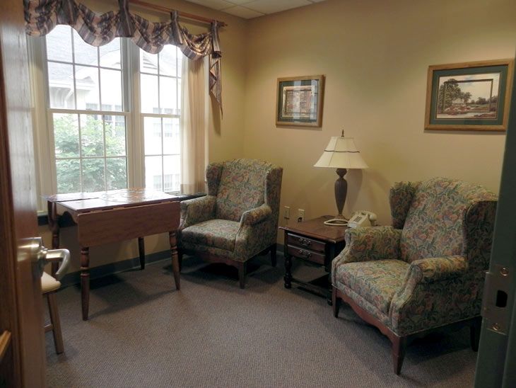 A cozy living room with two upholstered chairs, a side table with a lamp, and a window letting in natural light.