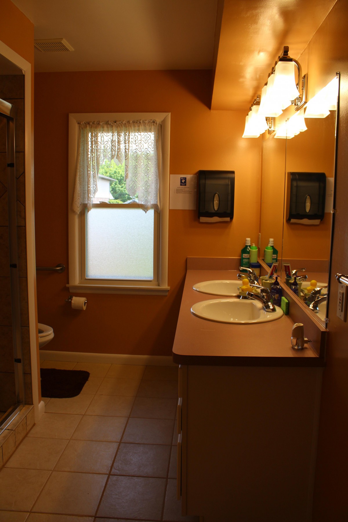A warm-toned bathroom featuring a double sink vanity with mirrors and overhead lighting.