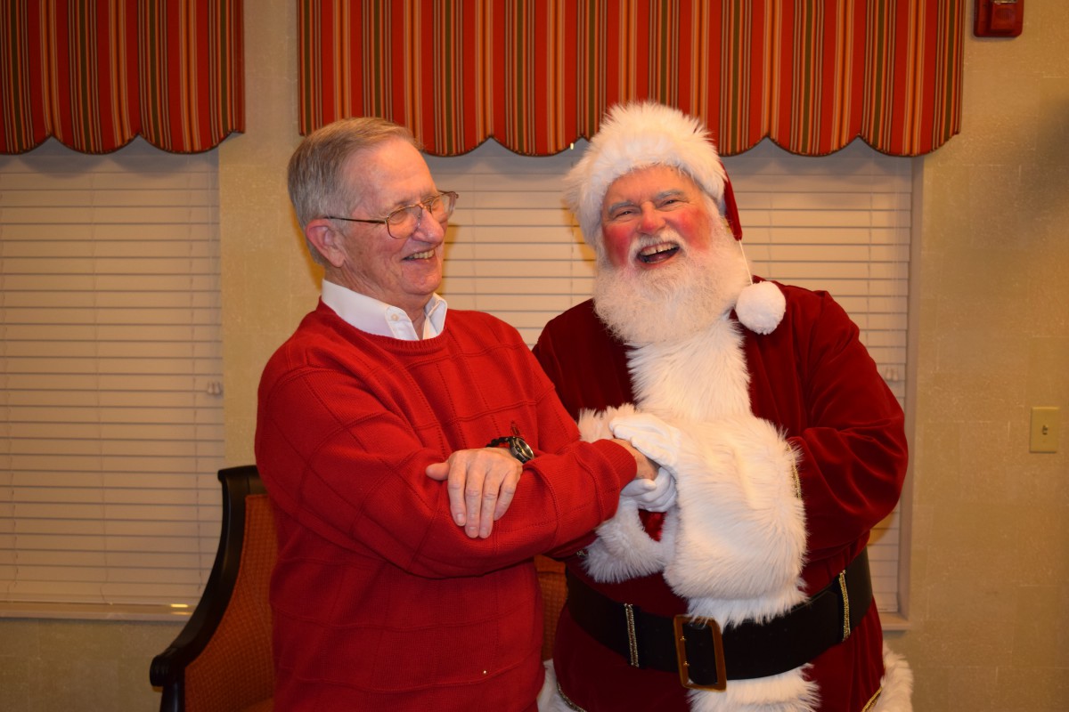Two men laughing together, one dressed as Santa Claus during a festive holiday gathering.