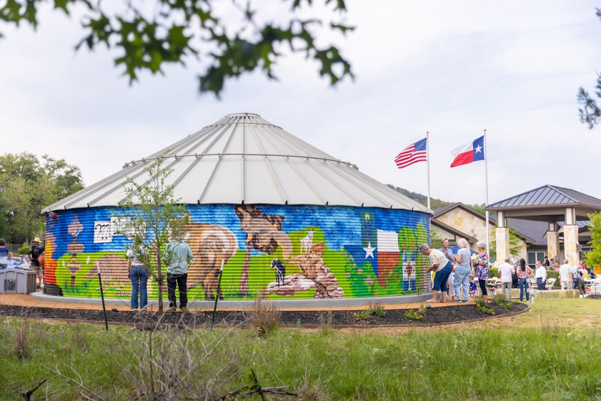 A mural painted on a silo with people gathered around, accompanied by American and Texas flags.
