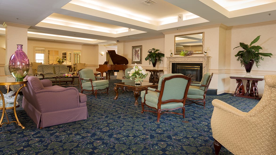 A cozy lounge area featuring a piano, armchairs, and a fireplace with traditional decor.