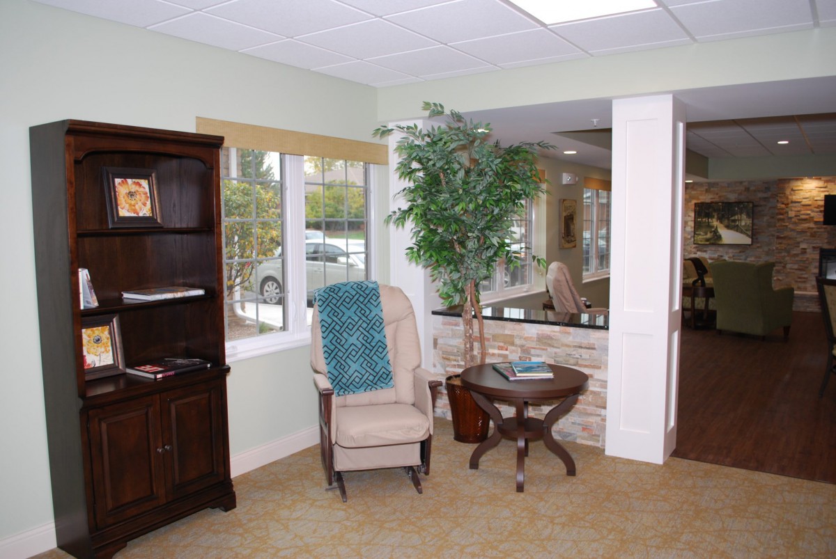 A cozy waiting room with a chair, bookshelf, and a potted plant by the window.