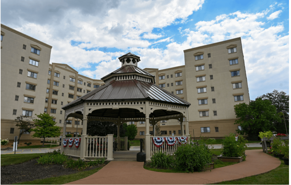 A gazebo surrounded by a tall building under a partly cloudy sky.