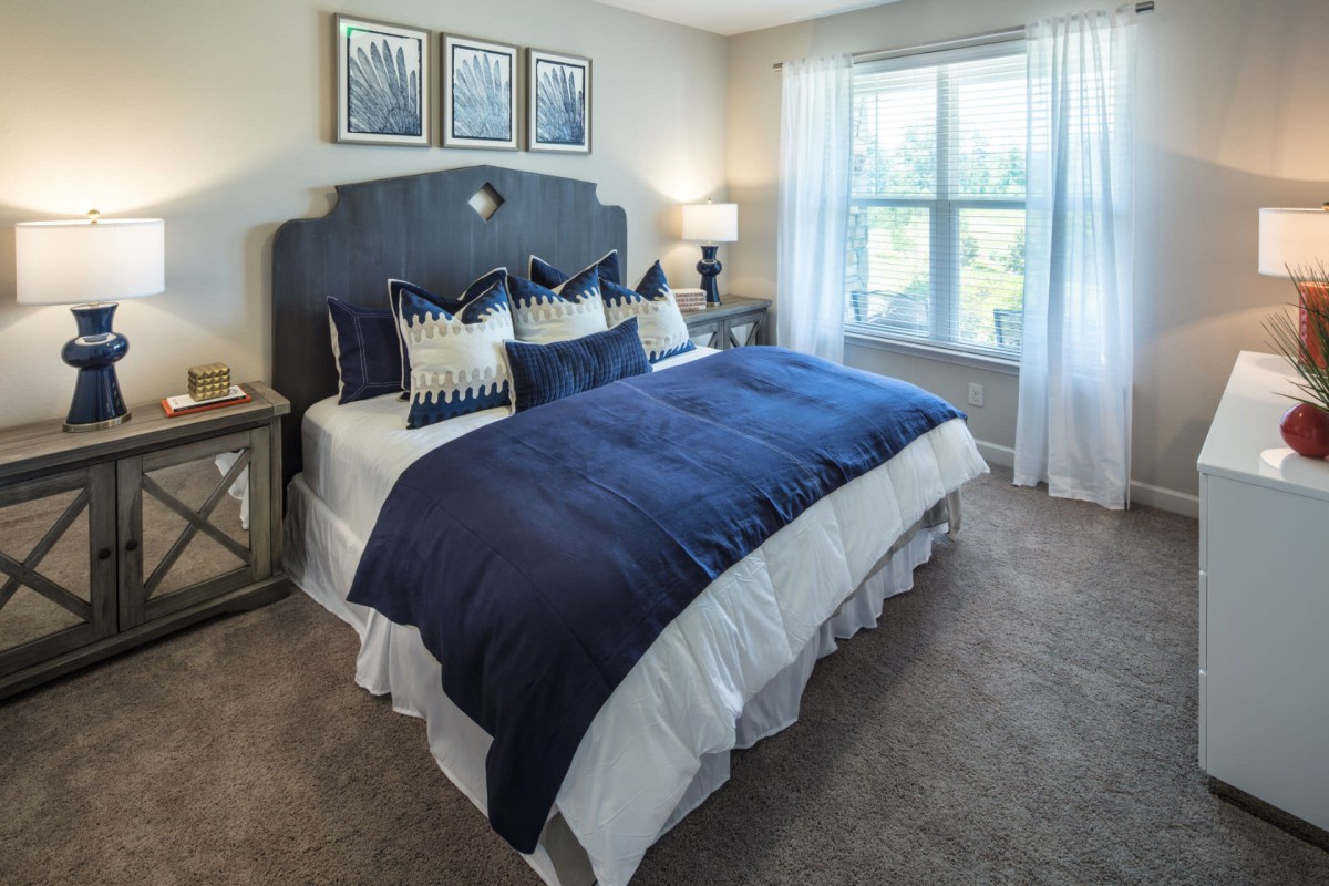 A cozy bedroom with a navy blue and white color scheme, featuring a large bed, decorative pillows, and natural light coming through the window.