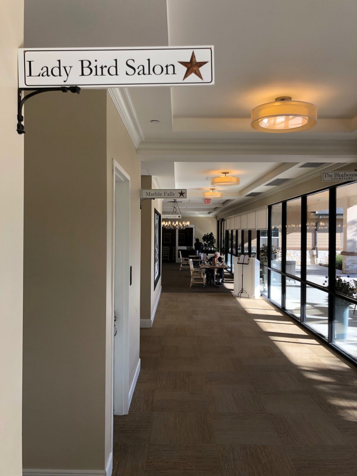 A corridor leading to the Lady Bird Salon, with large windows allowing natural light.