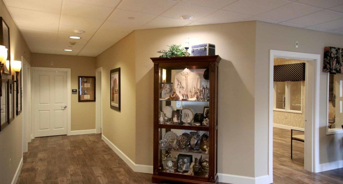 A well-lit hallway featuring a wooden display cabinet filled with decorative items and artwork on the walls.