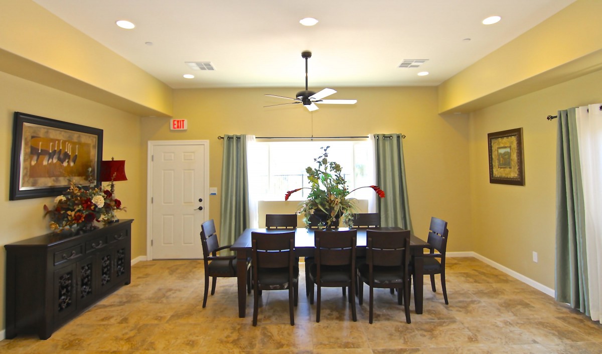 A spacious dining room with a large table, surrounded by chairs and lit by natural light streaming through the window.