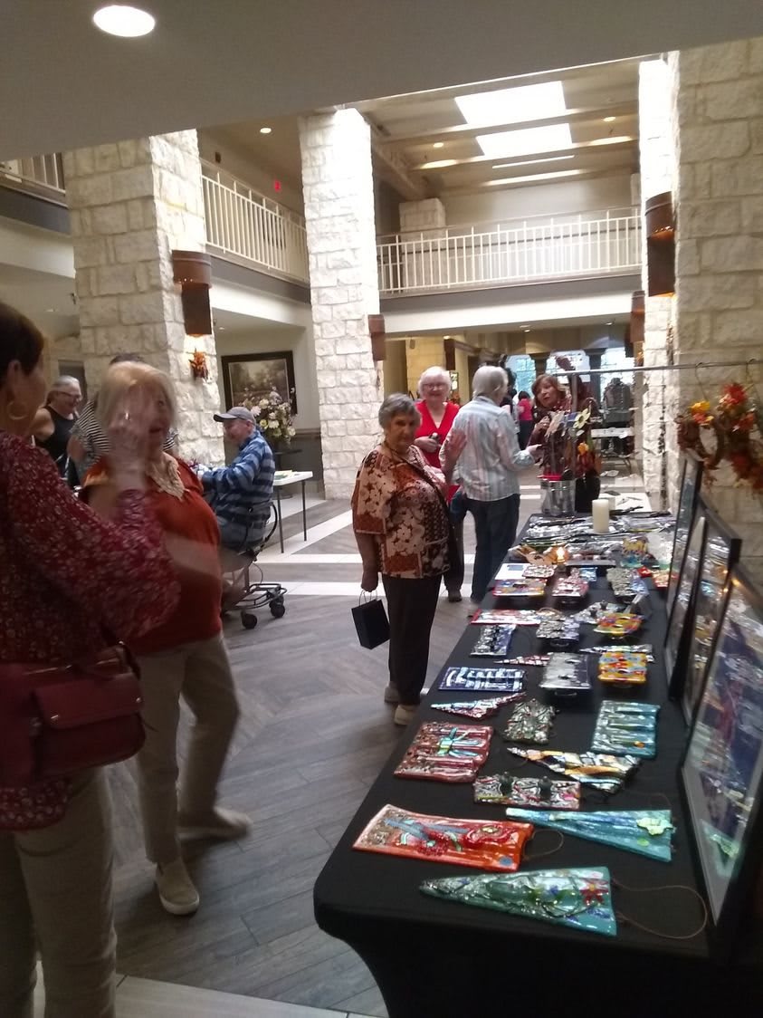 A group of people attending an indoor art exhibit with various artworks displayed on tables.