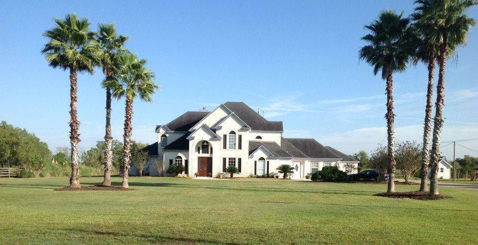 A luxury house with palm trees and a large lawn on a clear day.