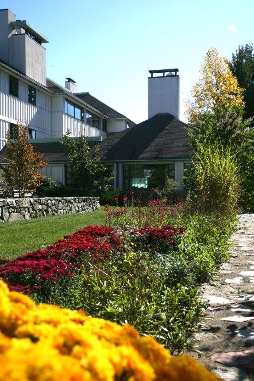 A scenic view of a landscaped garden with vibrant flowers and a stone pathway leading towards a modern building.