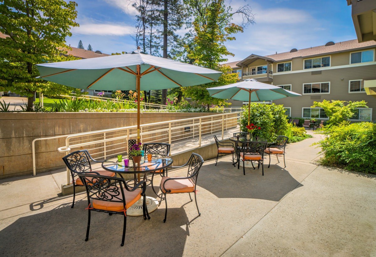 A sunny outdoor patio area with tables, chairs, and umbrellas in front of a building.