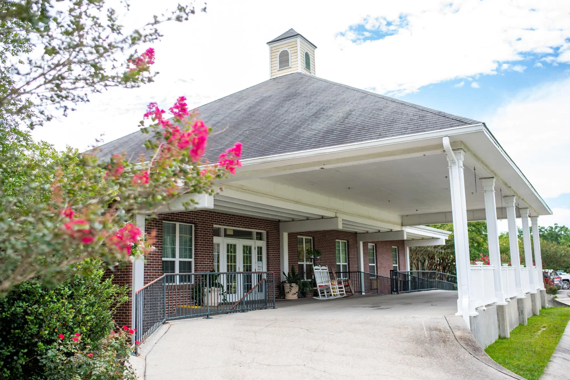 A building entrance with a covered porch surrounded by flowering plants.
