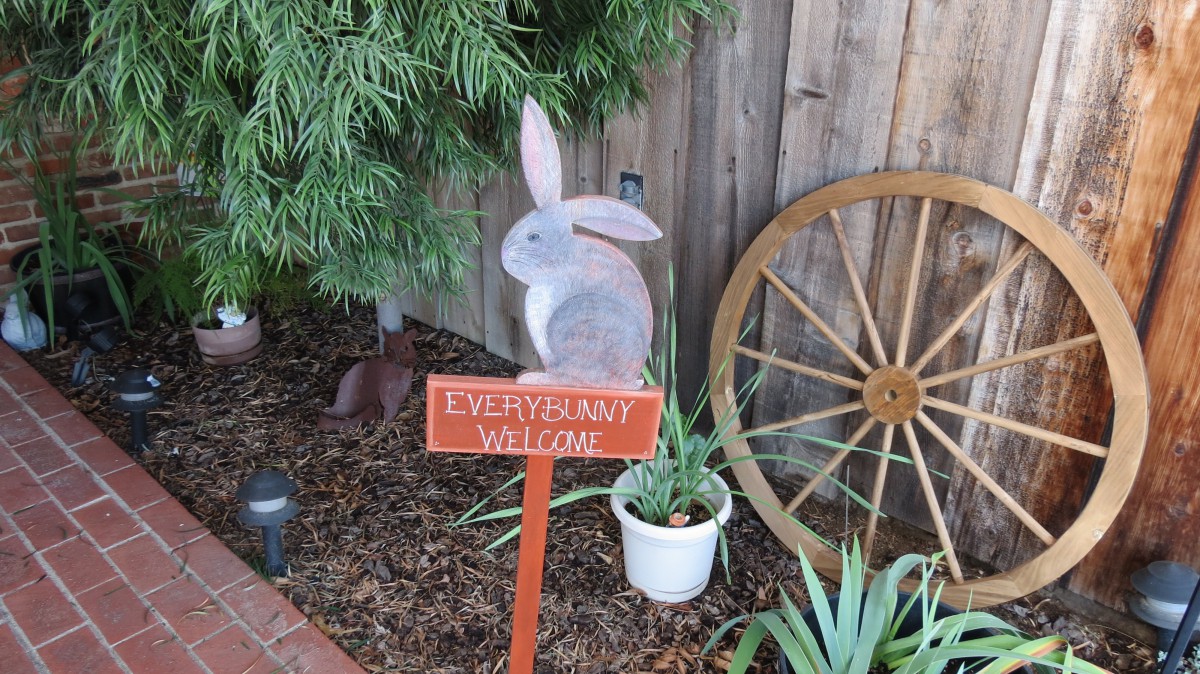 A garden scene with a wooden bunny, a sign reading 'EVERGREEN VILLAGE', plants, and a wagon wheel.