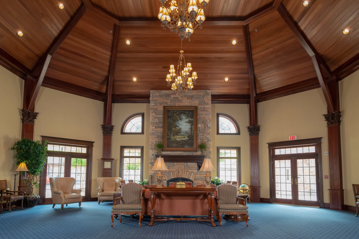 A spacious and elegant lobby with a high wooden ceiling, featuring chandeliers, comfortable furniture, and a fireplace.